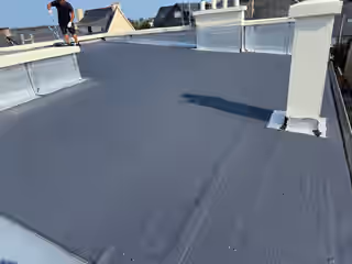 La même terrasse, membrane neuve d’un gris uniforme, un couvreur qui termine les relevés