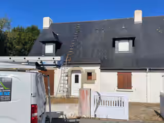 Maison bretonne à deux lucarnes, couverture d’ardoise grisée et tachée de lichen, le camion de l’entreprise devant