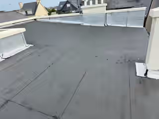 Toiture-terrasse à membrane bitumeuse délavée, joints ouverts et angles rapiécés