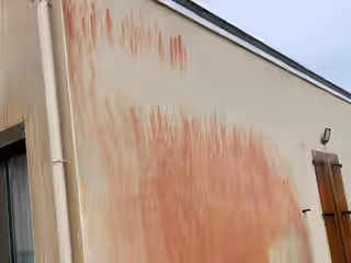 Pignon d’une maison couvert de coulures rouges d’algues sur toute sa hauteur