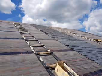 Pose de l’ardoise sur un grand pan de toiture, la couverture neuve qui avance à droite, deux échelles de couvreur posées à plat